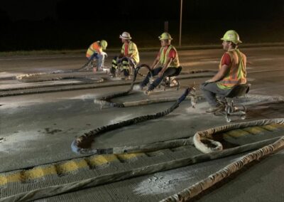 men injecting foam under road at night with truck lights glowing in the background