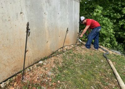 Workers doing deep foam injection along a concrete foundation